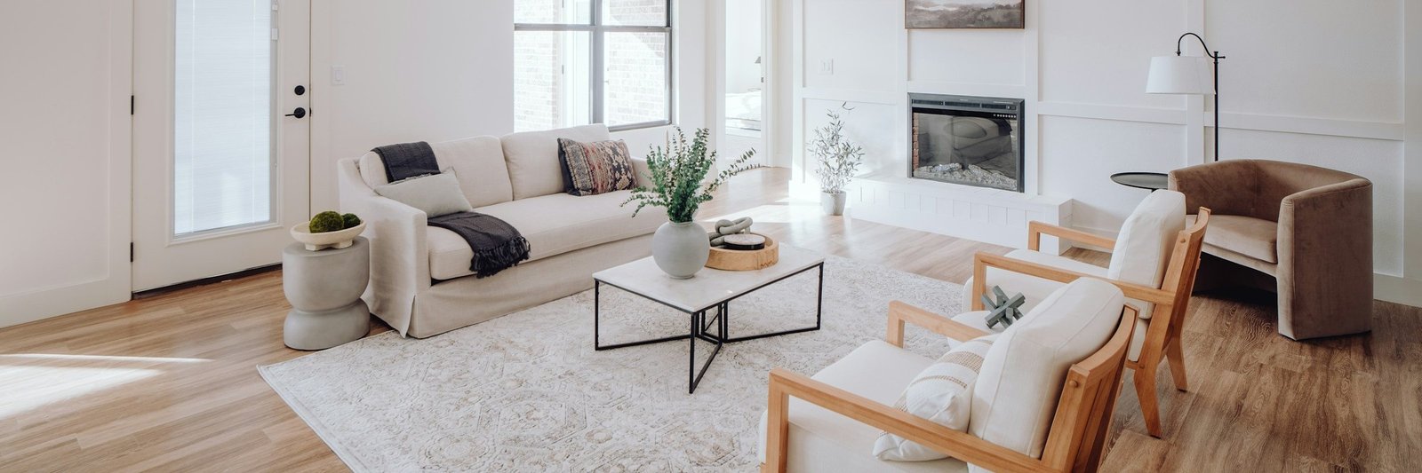 Bright living room with a cream sofa, wood accent chairs and a white paneled fireplace wall